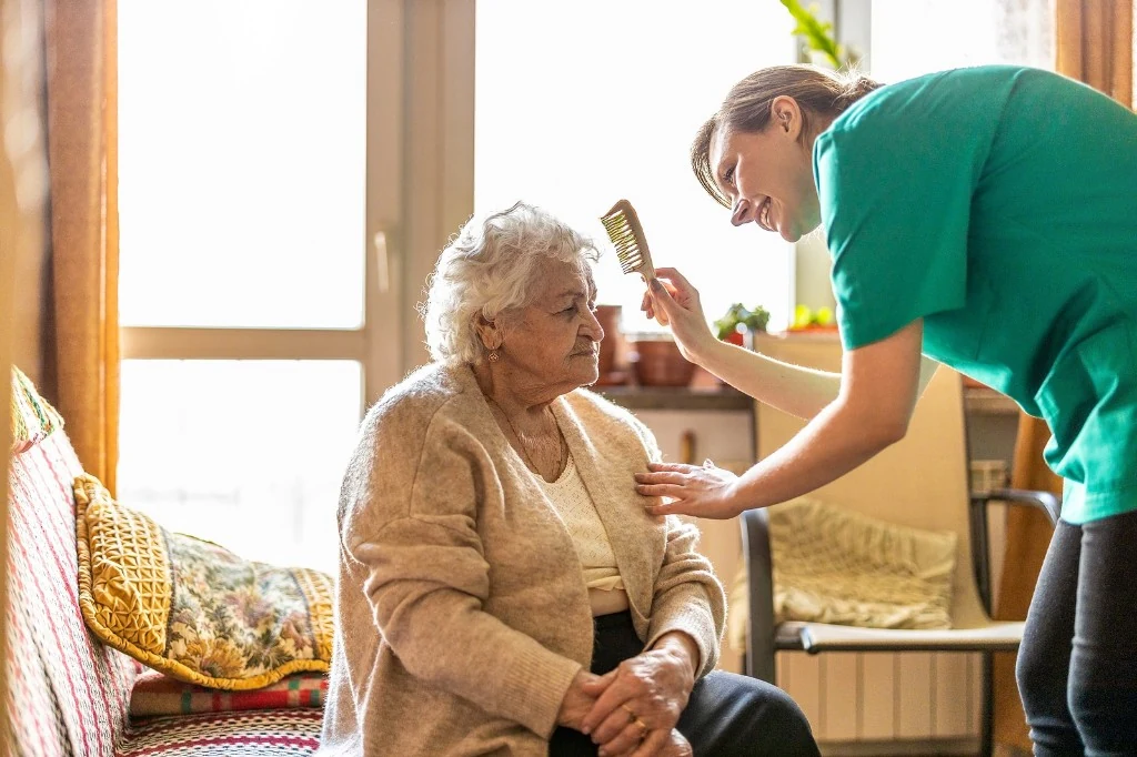 A caregiver gently helping a senior woman with grooming at home